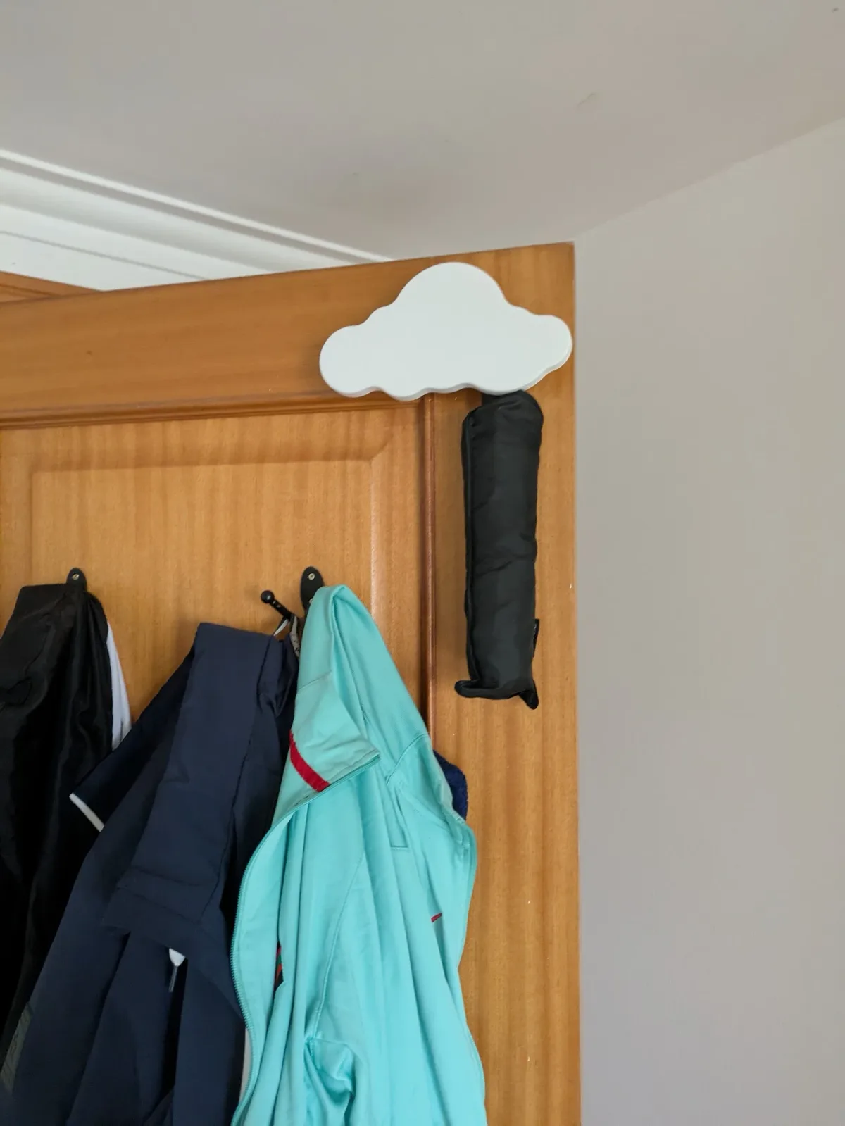 A white printed cloud clipped over the top of a door frame, with a folded black umbrella hanging beneath it.