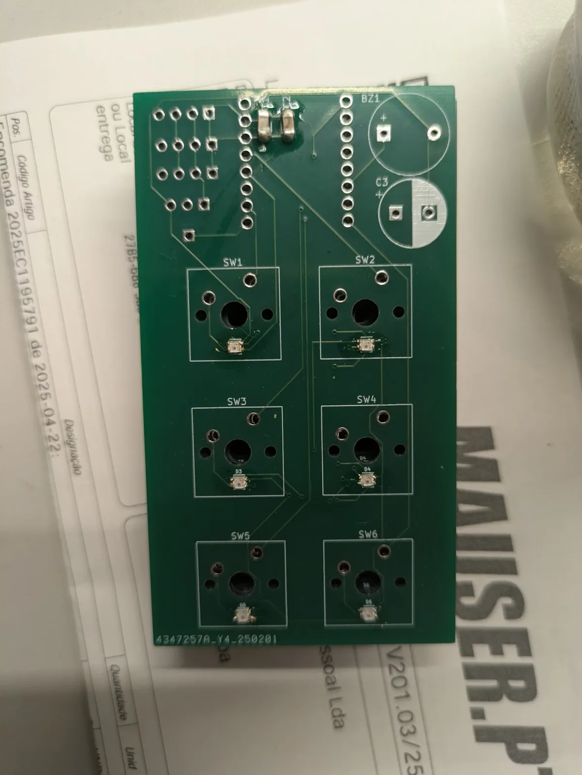 A bare green PCB with six labelled switch footprints, each with a small RGB LED beside it, plus a buzzer footprint and a pin header.