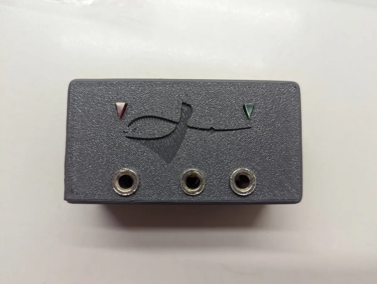 A grey 3D-printed box with a fencer engraved on the top face, a red and a green indicator, and three sockets along the front.