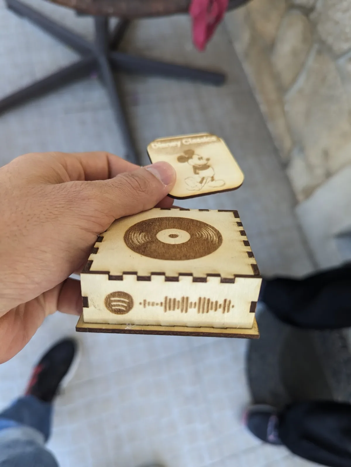 A small laser-cut plywood box with a vinyl record engraved on the lid and a Spotify code engraved on the front panel, held in one hand with a tag above it.